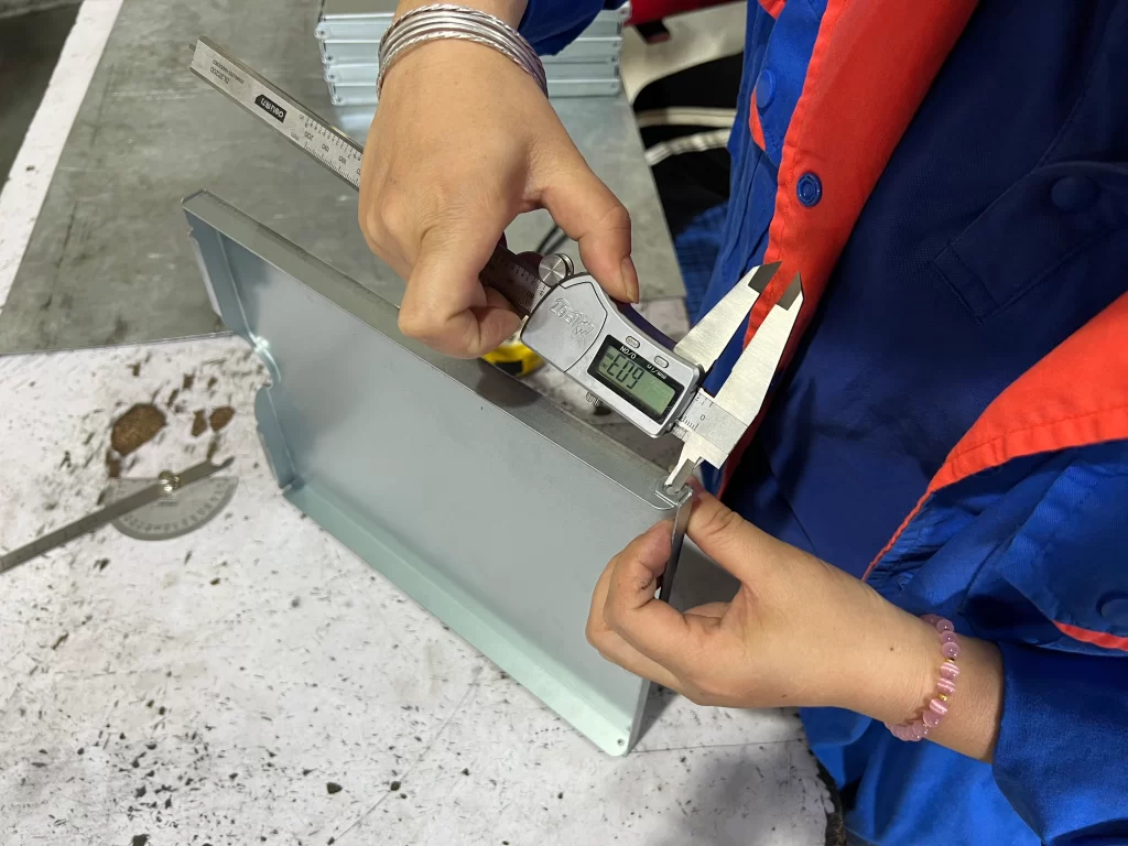 Quality inspector measuring a bent metal drawer panel with a digital caliper