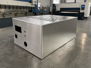 Custom stainless steel welded enclosure with brushed No.4 finish, precision bent corners and smooth weld seams, displayed on factory workbench with sheet metal workshop background